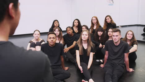 teacher at performing arts school talking to students sitting on floor in rehearsal studio