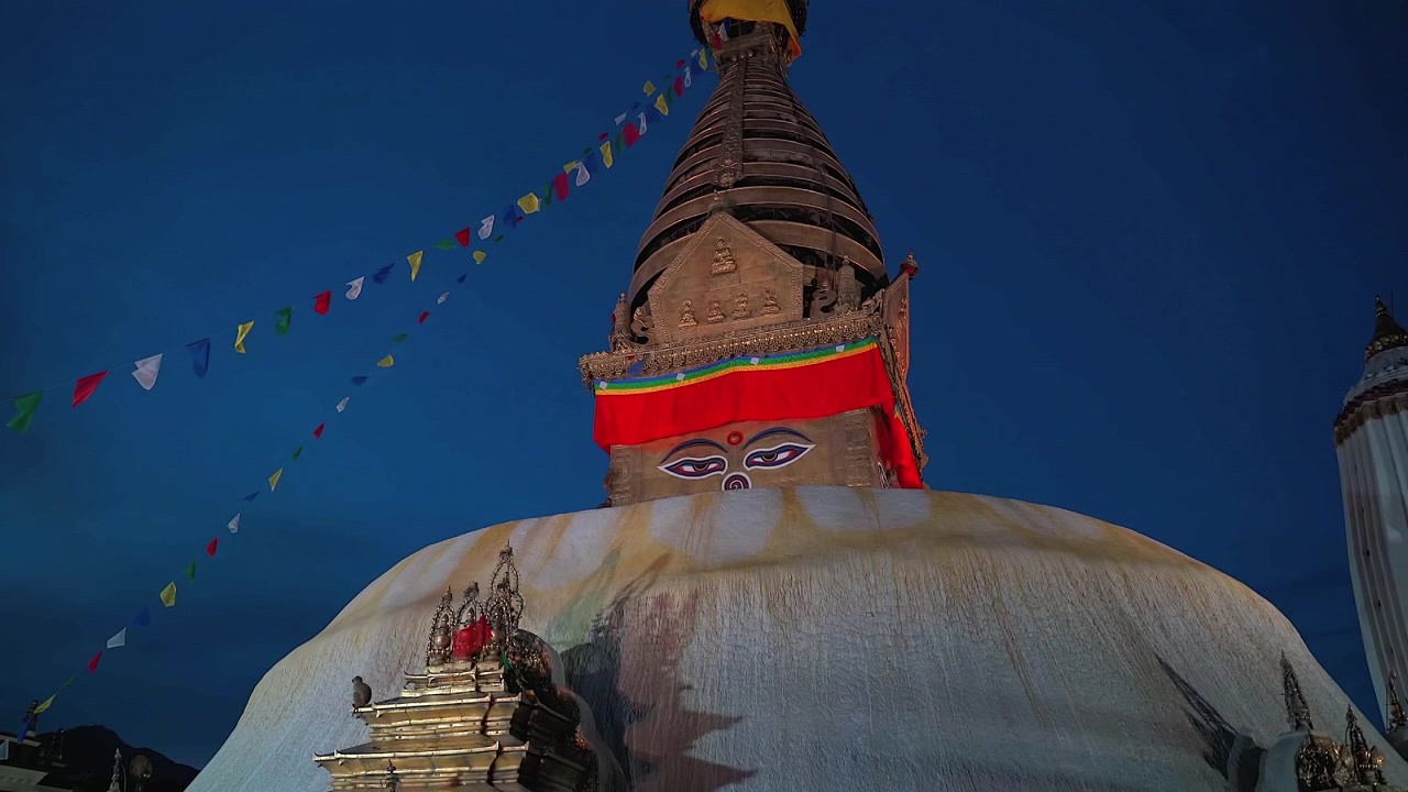 Et statisk mellembillede i lav vinkel af den hellige Swayambhunath Stupas gyldne spir med Buddhas malede øjne under en dybblå skumringshimmel i Kathmandu, Nepal.