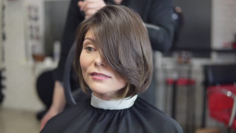 ein professioneller friseur zeigt einen kurzen haarschnitt mit spiegel an einen hübschen zufriedenen weiblichen kunden in einem professionellen friseursalon.