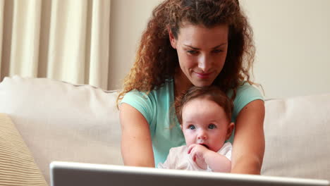 madre usando una computadora portátil con el bebé en el regazo