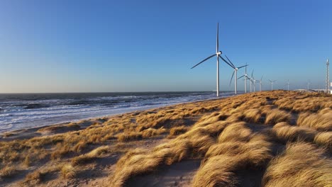 vista en cámara lenta sobre las dunas de color naranja mientras los molinos de viento giran en el viento