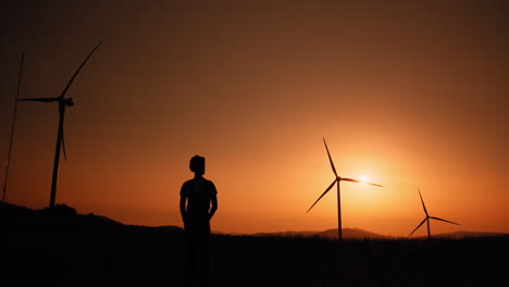 silhouette of a person watching the sunset with wind turbines in the background