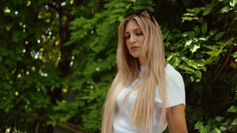 an attractive young woman at a railing in a park. blonde and young. slow motion, alone.