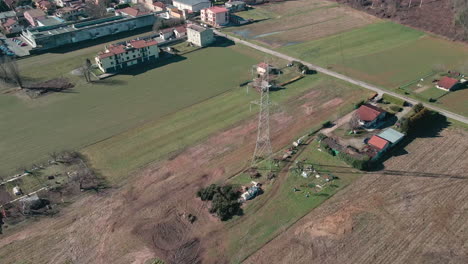 vista panorámica del campo desde arriba con campos de agricultores, casas residenciales y torre de alto voltaje con cables eléctricos en arcore, norte de italia - dron aéreo, plano general