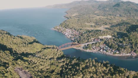 Goldene-Metallbrücke-überspannt-Das-Ruhige-Blaue-Wasser,-Das-Das-Kleine-Fischerdorf-Und-Die-üppigen-Berge-Mit-Grünen-Kokospalmen-Im-Südlichen-Leyte,-Philippinen,-Verbindet