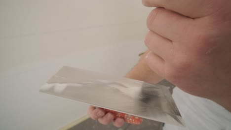 man plastering the walls with finishing putty in room with putty spatula