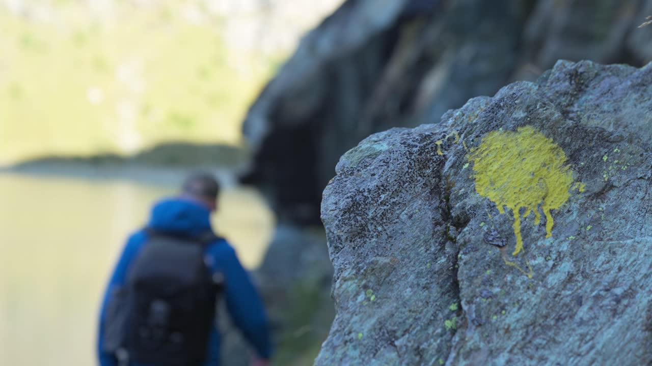 Hiker walking past trail sign along cliff and mountain lake