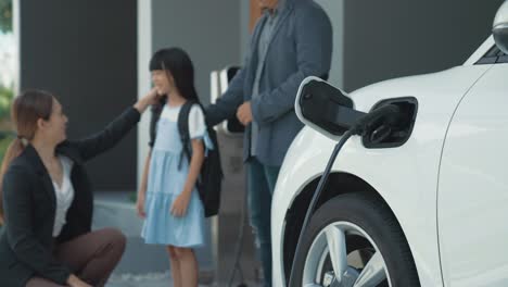 familia progresista con coche ev y estación de carga prepara a su hija para la escuela.
