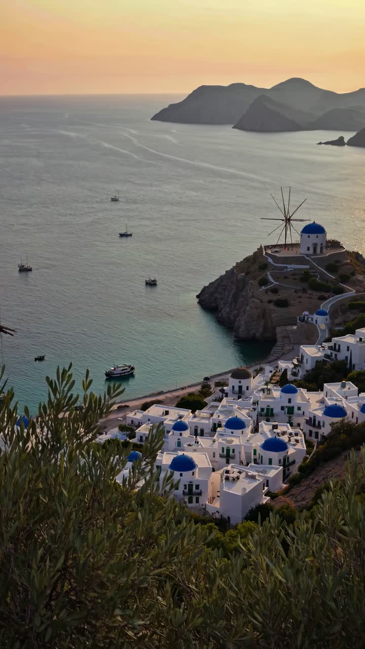 Aerial view of a coastal village with white buildings and blue domes at sunset, capturing a serene
