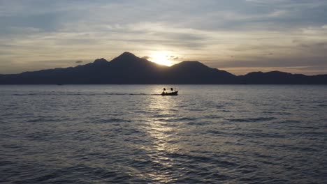 Fishing-Boat-heads-out-to-ocean-at-sunset-against-a-beautiful-Mountainous-Landscape-in-Asia