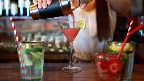 Mid-section-of-barmaid-pouring-cocktail-in-glass-at-bar-counter