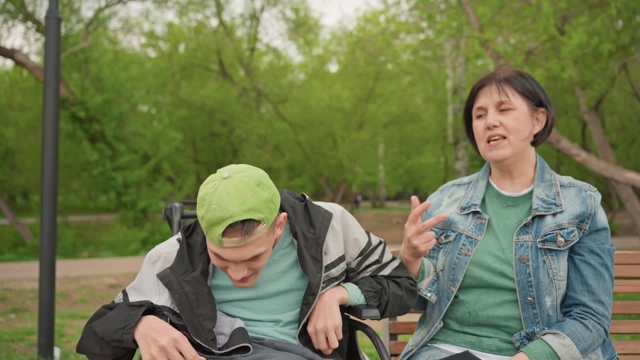 Engaging Hand Movements Outdoors, Expressive Exchanges On Park Bench During Pleasant Spring Day, Vivid Communication Through Animated Gestures Between Caregiver And Young Man In Outdoor Setting