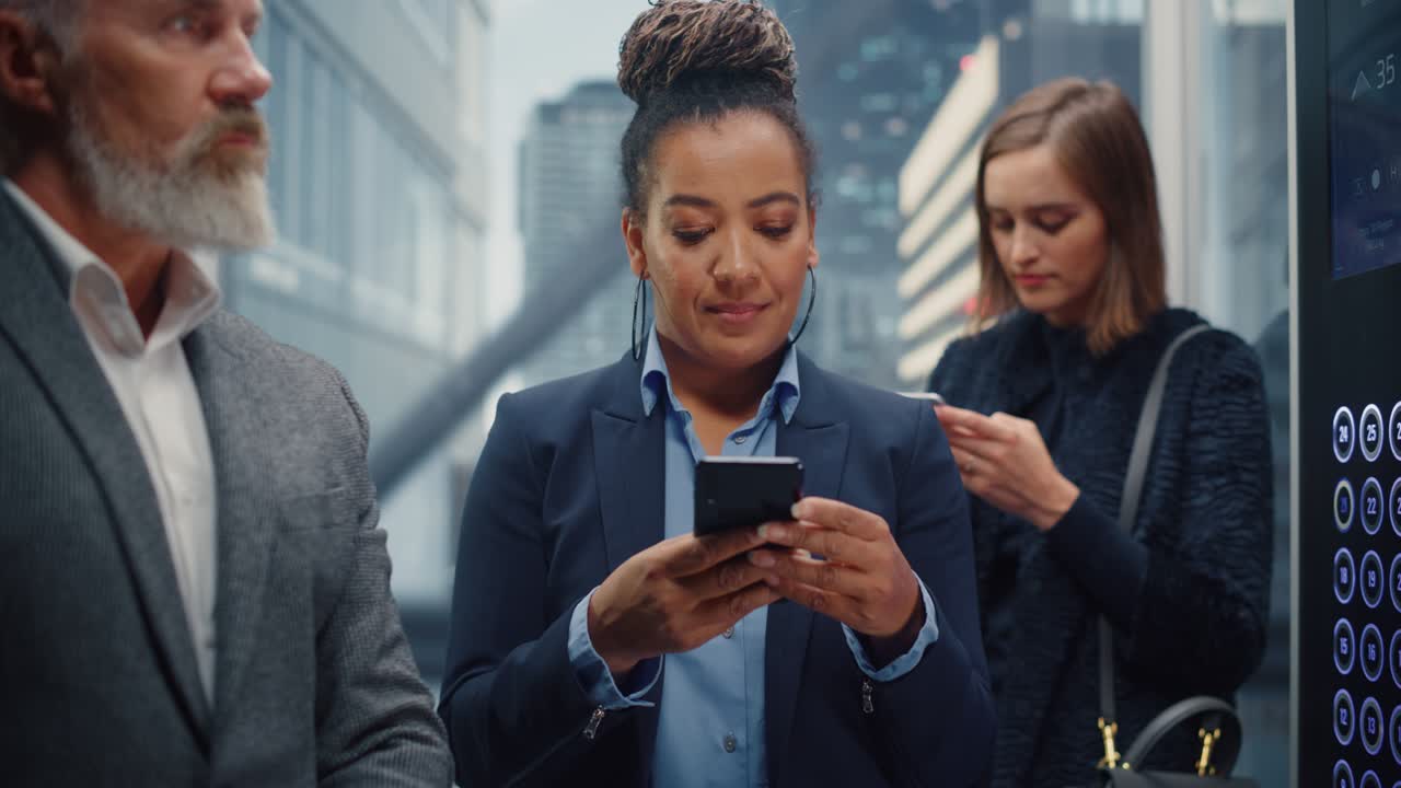 Beautiful Black Adult Female Riding Crowded Glass Elevator to Office in Business Center. Successful African American Manager Using Smartphone, Write Message, Check Social Media and Emails in a Lift.