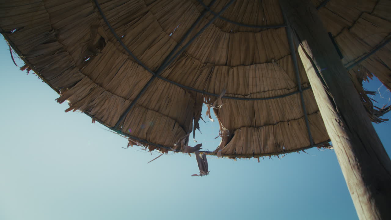 Static upward shot of straw sunshade gently blowing in wind against clear sunny blue sky at Elafonisi Crete