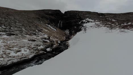 Drone-Flying-In-Iceland-With-Beautiful-Nature-Scenic-of-A-Water-Falls,-Stream-Water-Flowing-And-Landscape-Covered-With-Snow---Aerial-Shot