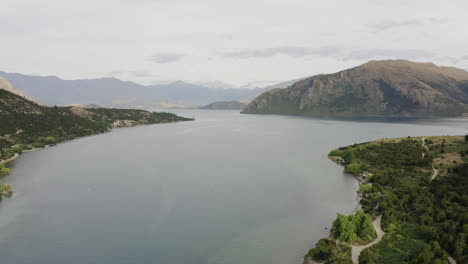 Seguimiento-Aéreo-Del-Lago-Wanaka-En-Una-Mañana-Aún-Nublada-En-El-Centro-De-Otago-Mientras-Las-Montañas-Se-Sientan-Al-Sol