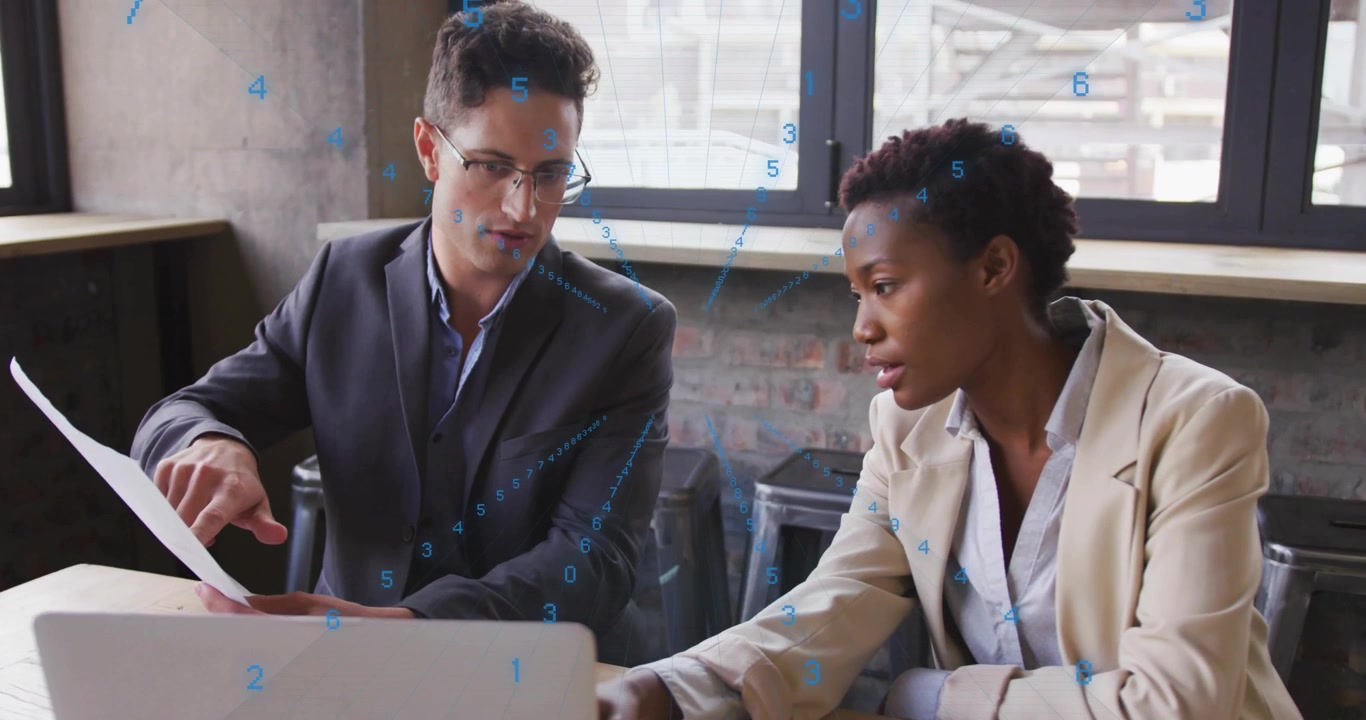 Após um homem apontar para uma seção de relatório, uma mulher navega no laptop analisando tendências de dados empresariais.