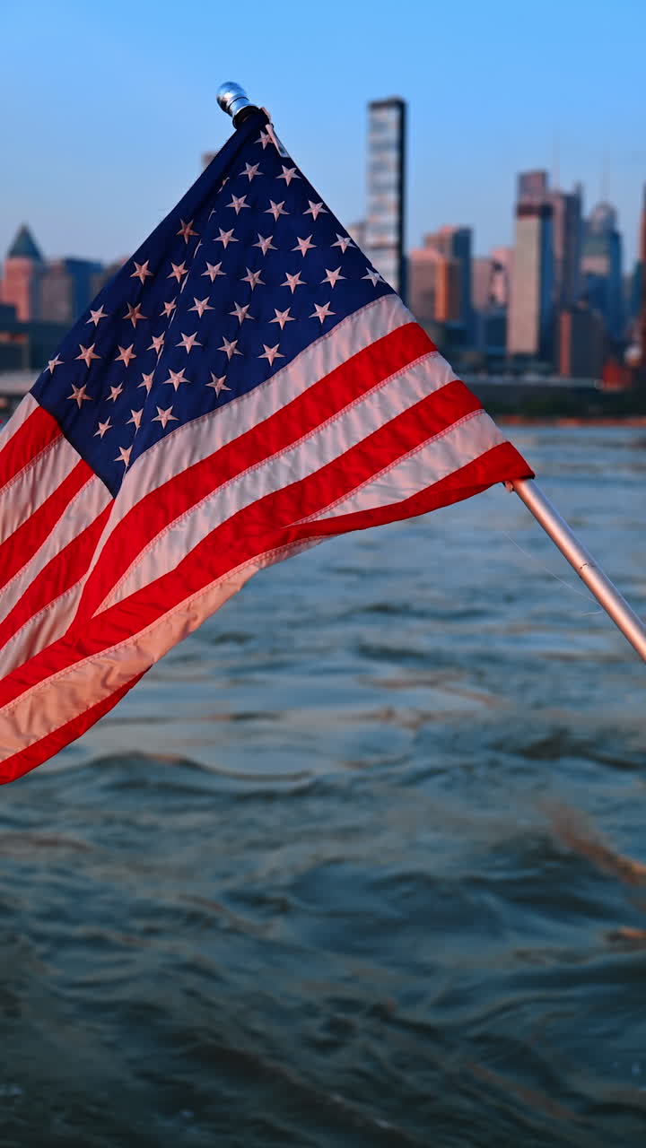 Bandiera americana che sventola alla luce del tramonto. Primo piano. Paesaggio acquatico e skyline della città sullo sfondo. Video verticale