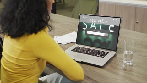 biracial woman at table using laptop, online shopping during sale, slow motion