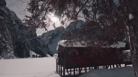 Snow-capped-wooden-hut-by-frozen-Lake-Braies,-Dolomites-winter-scenery