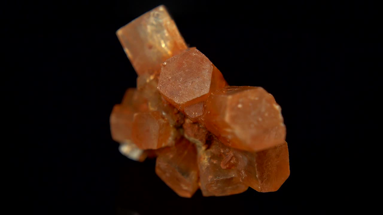 검은색 배경 앞에 혈색 오렌지 광물 (아라고나이트) 을 원활하게 회전시니다.