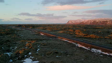 drone aerial shot on typical iceland landscape with a road in the middle, red sand, red mountains green ground and snow