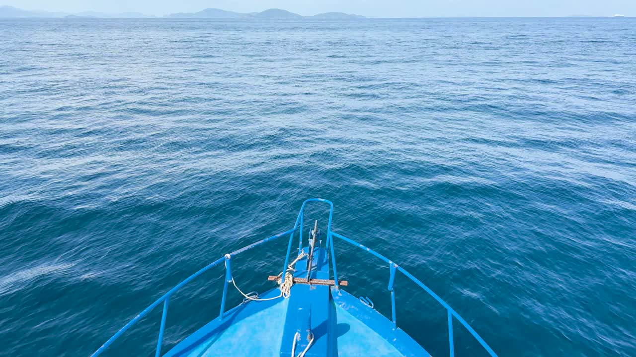 A boat glides smoothly over calm ocean waters near Phuket, Thailand, under clear skies and bright sunlight