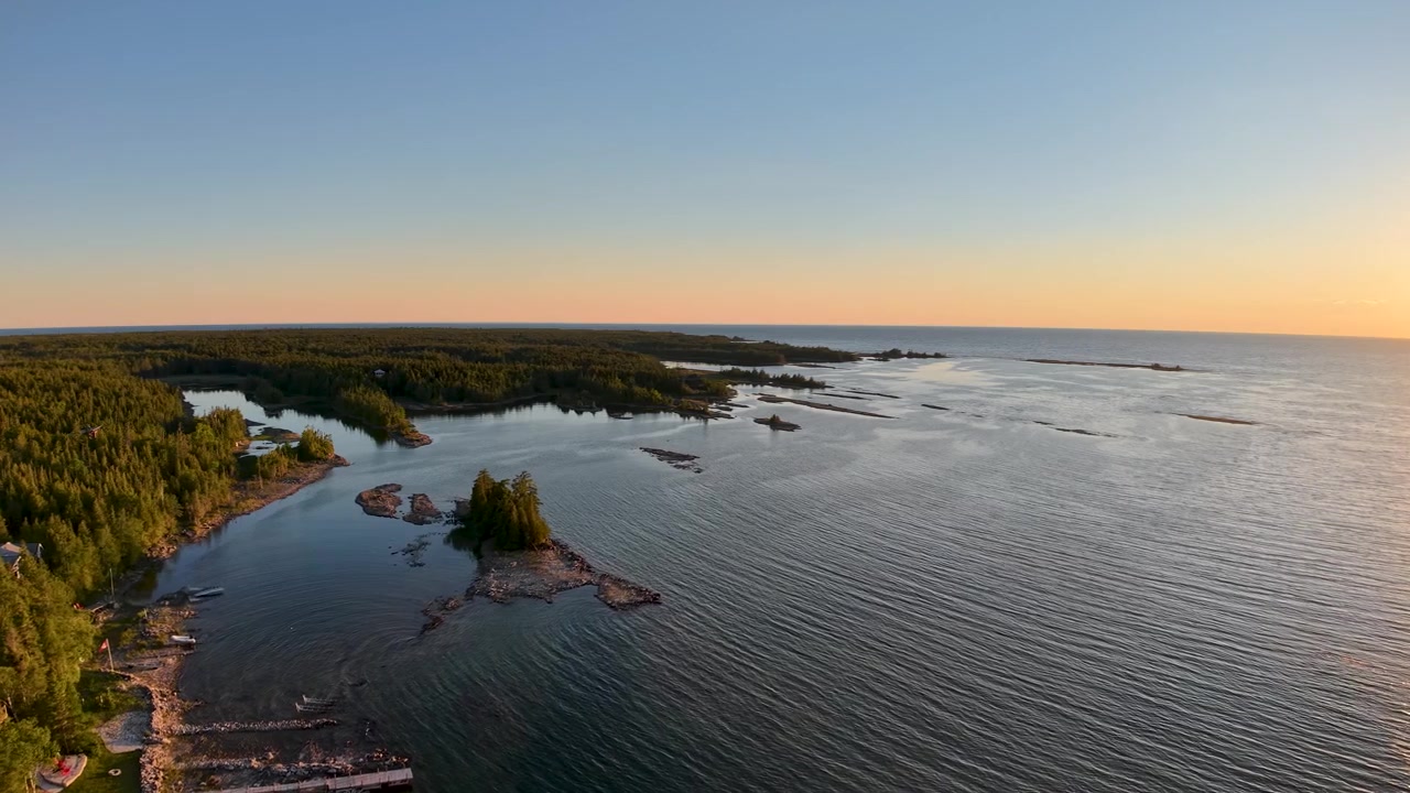 Laskeva aurinko paistaa avoimen Huronjärven yli karun metsäisen Tobermoryn rannikon vieressä.