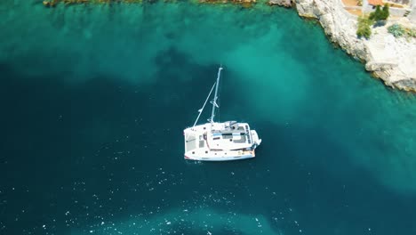 Yates-A-La-Deriva-En-La-Bahía-Cerca-De-La-Ciudad-Costera-De-Croacia-Contra-El-Telón-De-Fondo-De-Cielos-Azules-Y-Agua-Azul-Transparente