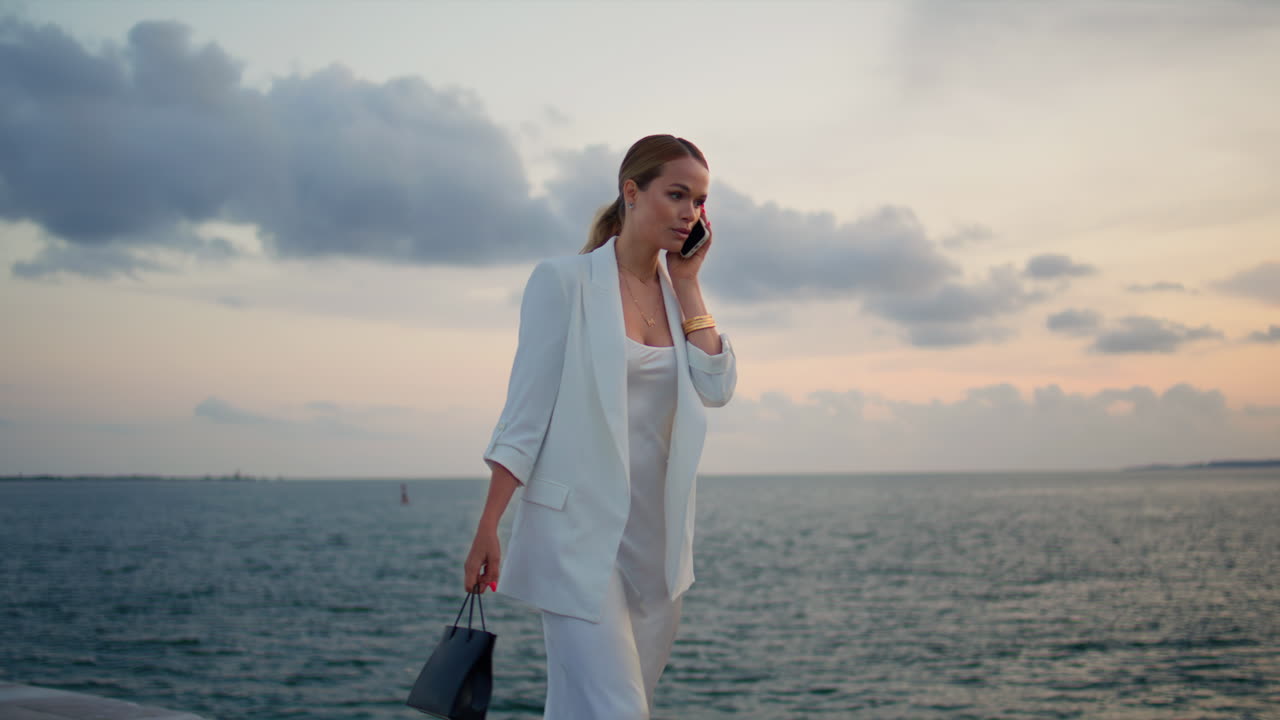 해가 지는 하늘에서 부르는 우아한 여인. 스마트폰을 사용하는 여인이 을 고 있다.