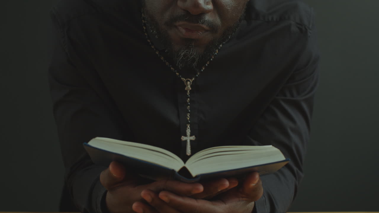 Duchovní drží otevřenou Bibli a nahlas čte modlitbu