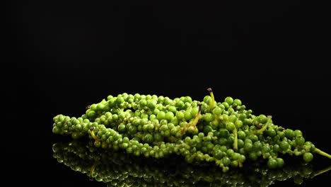 a cluster of fresh green peppercorns rotates smoothly on a reflective black surface, illuminated by dramatic studio lighting for a vivid, high-contrast effect