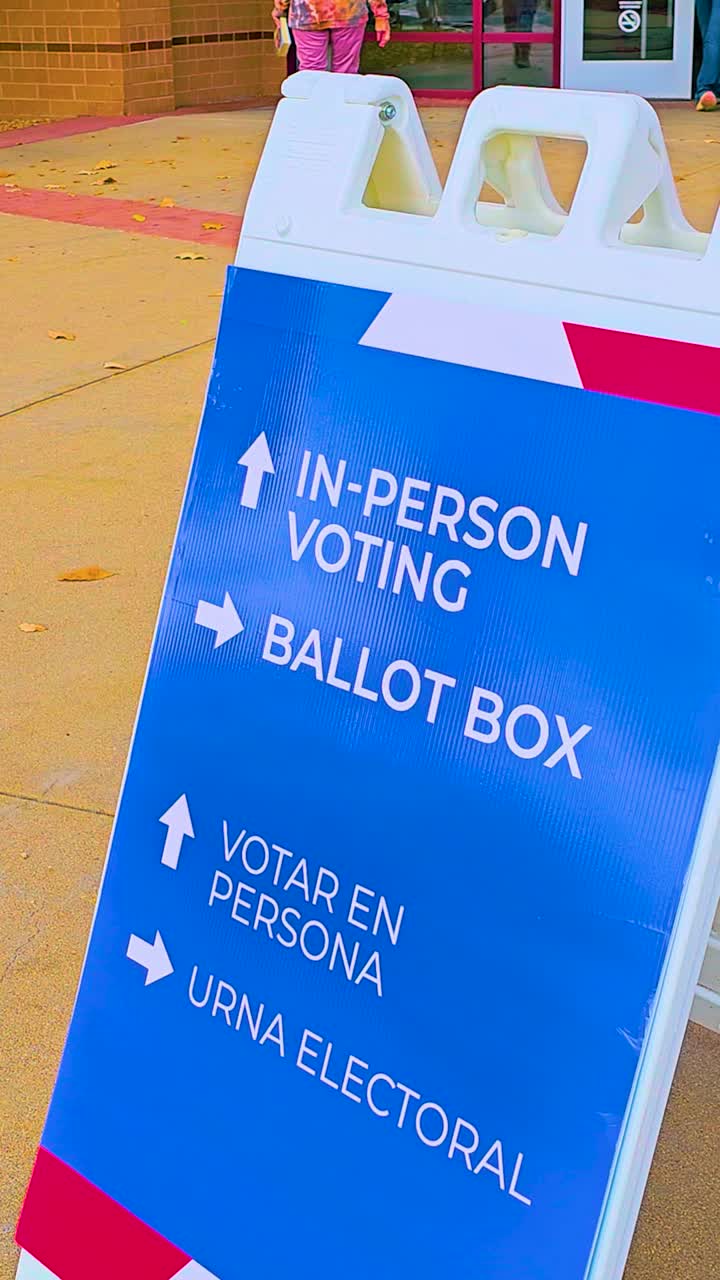 Pedestrians pass in the background as a ballot drop-off sign with arrows includes Spanish text Votar en Persona and Urna Electoral, emphasizing civic duty, accessibility, trust and integrity. Vertical
