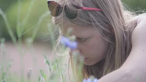 blonde female sitting down among flowers to take photos with her phone