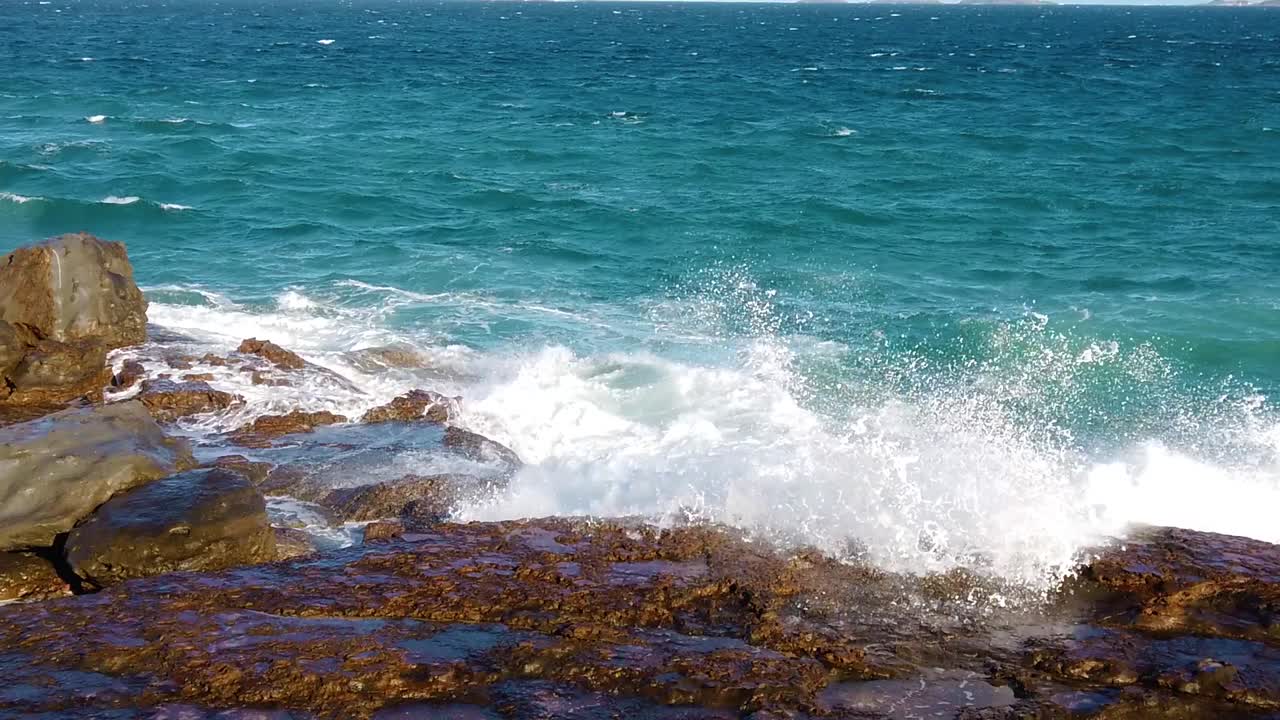 바위가 있는 해변에 파도가 부히고 바위 위에 물이 아주 느린 속도로 어집니다.
