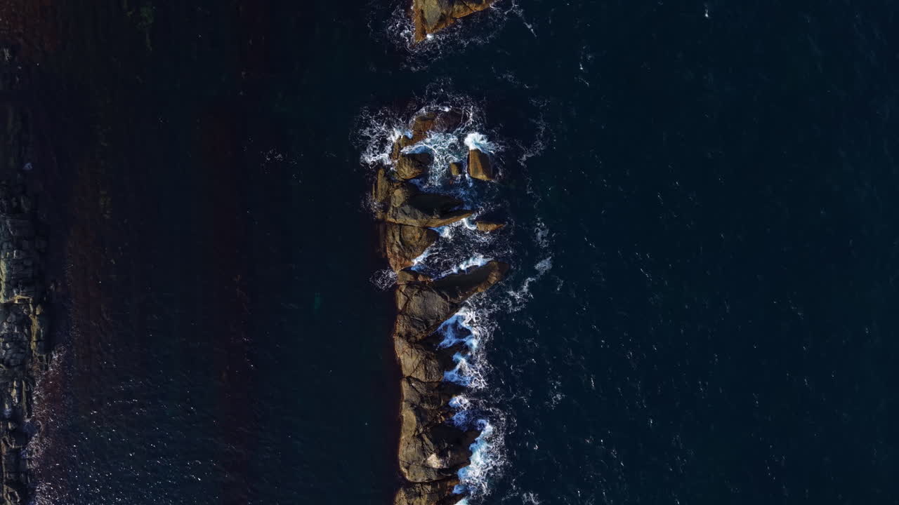 Waves crashing against jagged rocks along a tranquil coastline at sunset, capturing the beauty of nature's raw power and serenity