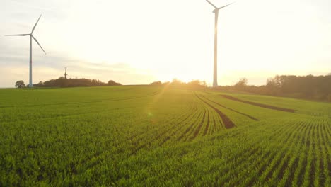 Vuelo-De-Drones-Sobre-Campos-Verdes-Con-Turbinas-De-Viento-Hacia-El-Amanecer