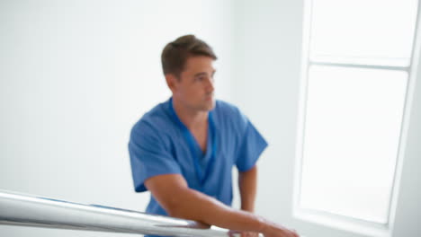 Portrait-Of-Smiling-Young-Male-Doctor-Or-Nurse-Standing-On-Stairs-In-Hospital