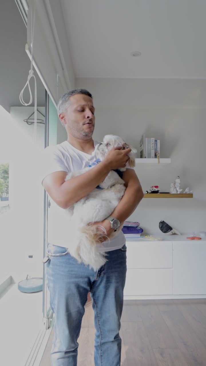 Uomo che tiene in braccio e accarezza il suo cagnolino al chiuso