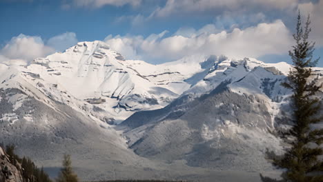 cinemagraph of white clouds in blue sky moving over snowcapped mountain range and treetops