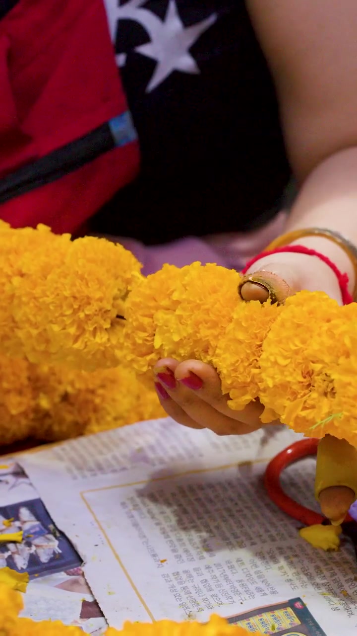Primo piano di mani artigiane che intrecciano calendule gialle in una ghirlanda tradizionale al Mercato dei Fiori di Bangkok.