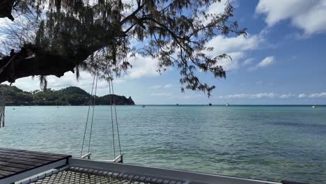 Terraza-De-Hotel-De-Lujo-Con-Hamaca-Y-Columpio-De-Madera-En-La-Costa-De-Una-Isla-Paradisíaca-Tropical,-Con-Vistas-Al-Horizonte-De-Aguas-Tranquilas-Y-Claras-Del-Océano.