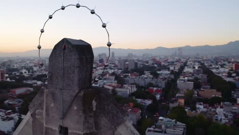 dramatic cinematic wide drone shots of massive jesus status towering over mexico city at sunset, featuring parroquia del purism corazon de maria and the sun setting over mountains and buildings