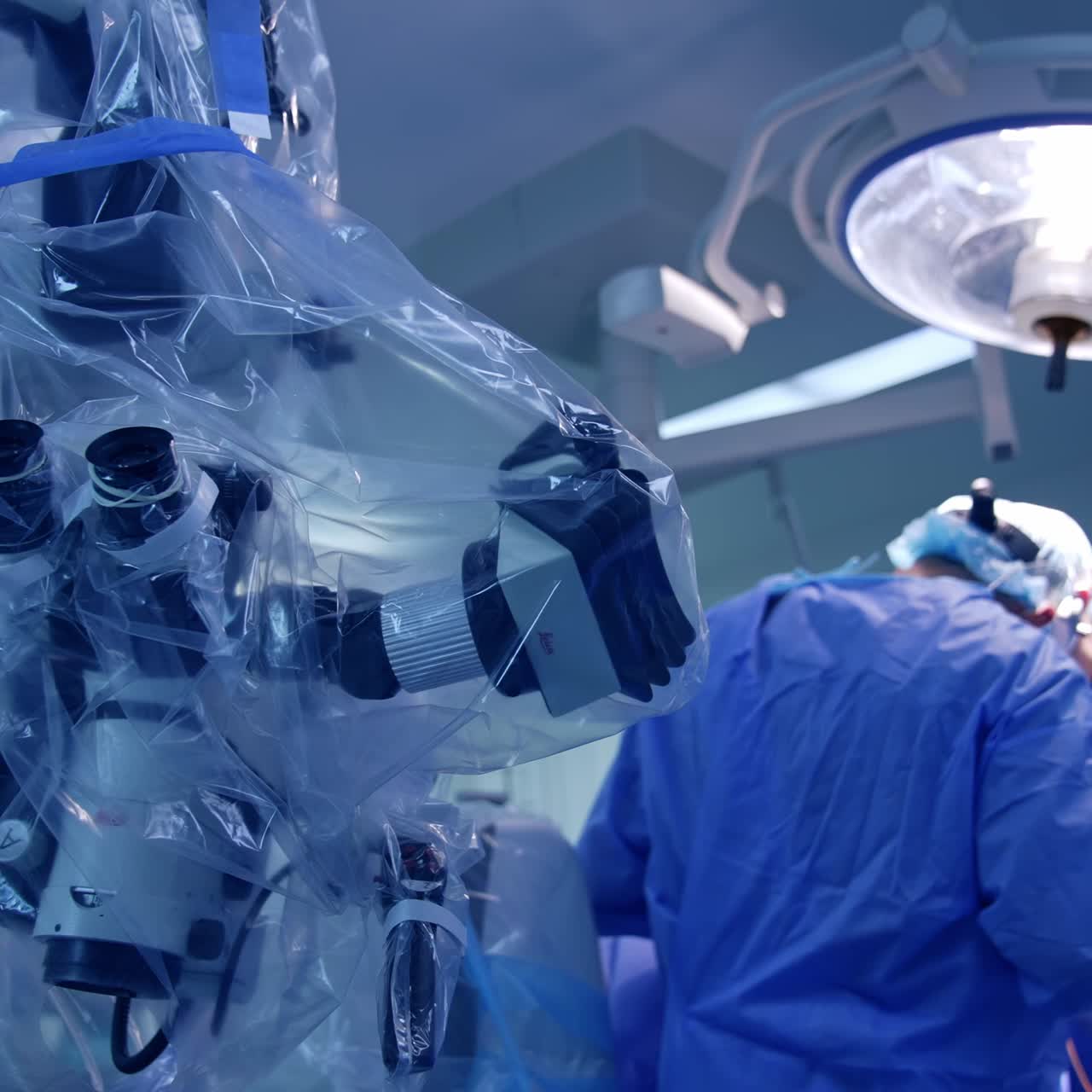 Technological microscope covered with plastic in surgery room. Close up. Rear view of surgeons working at operational table