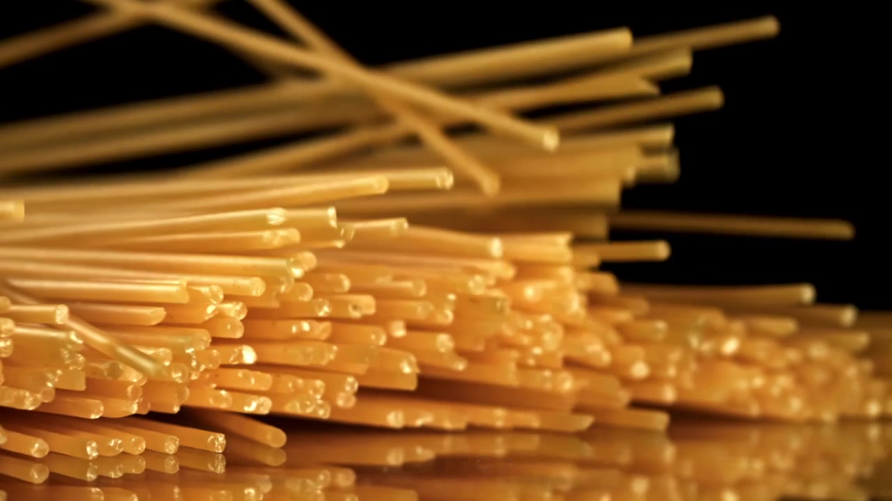 Spaghetti secchi che cadono su sfondo nero.