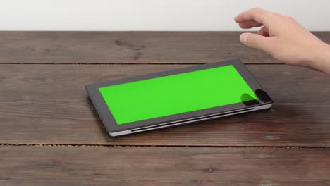una tableta con una pantalla verde en una mesa de madera, hace un pergamino con un dedo.