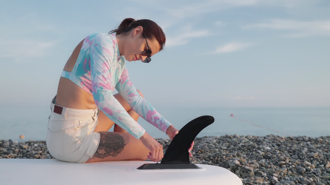 mujer instalando la aleta de la tabla de surf en la playa