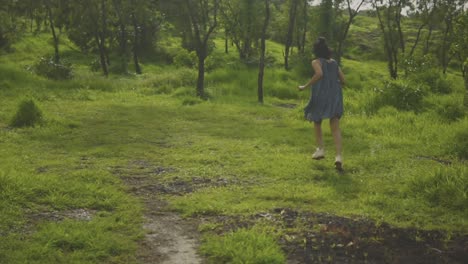 Women-in-blue-dress-running-towards-the-trees-in-an-open-grassy-woodland-on-a-warm-spring-day