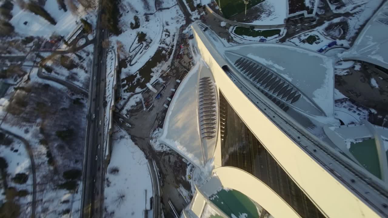 FPV aerial view of Olympic Stadium at sunset with snow-covered rooftop on a winter day
