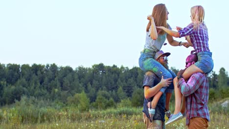 two blonde happy girls sitting on the shoulders of their multiethnic boyfriends and having fun at the holi holiday